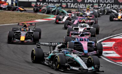 Multiple Formula 1 cars race closely around a curve; Mercedes leads with TAG Heuer banners in the background.
