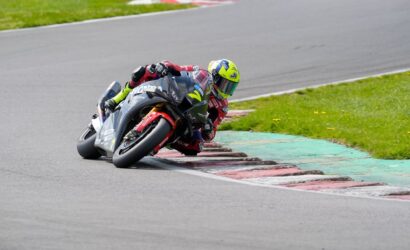 Motorcycle racer in a neon helmet leaning into a corner on a race track, mid-turn.