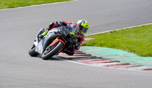 Motorcycle racer in a neon helmet leaning into a corner on a race track, mid-turn.