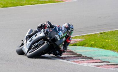 Motorcycle racer in full gear leans into a corner on a race track.