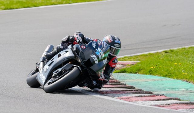 Motorcycle racer in full gear leans into a corner on a race track.