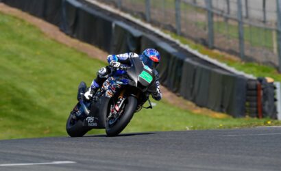 Motorcycle racer in blue gear leaning into a turn on a race track, black bike with green '52' number plate.
