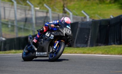 Motorcycle racer in a pink helmet leans into a turn on a race track, blue and black bike numbered 28 in view