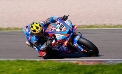 Motorcycle racer in blue-red suit leaning into a turn on a racetrack, yellow helmet visible, blue race bike number 56.](https://)