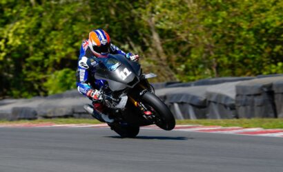 Motorcycle racer in blue gear and orange helmet leans into a turn on a race track.