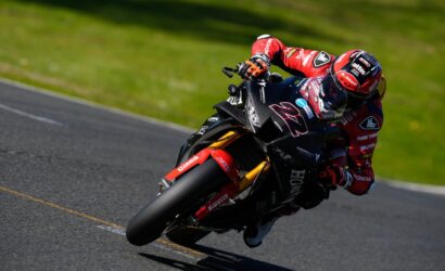 Motorcycle racer in red gear leaning into a corner on a racetrack, bike number 27.