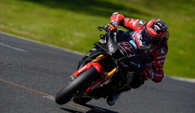 Motorcycle racer in red gear leaning into a corner on a racetrack, bike number 27.