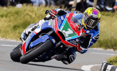 Racing motorcyclist leaning into a right-hand curve on a blue-and-red sport bike in full gear with a neon helmet.