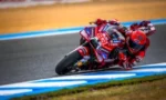 Motorcycle racer in red gear leaning into a turn on a race track in a sharp corner moment.