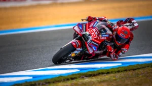 MotoGP rider in red leathers leaning into a sharp turn on a race track.