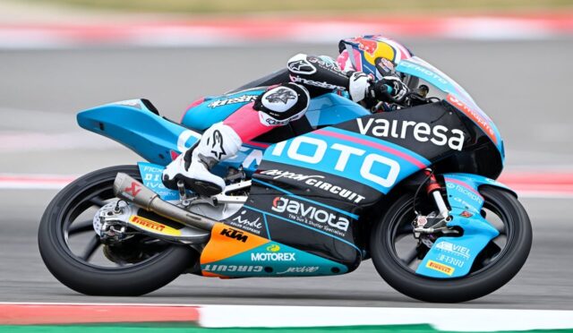 Motorcycle racer leaning into a high-speed turn on a blue race bike with sponsor logos.