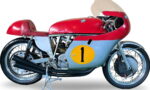 Vintage racing motorcycle with red top, blue side panel, and a yellow number 1 decal on the side panel, on a stand.