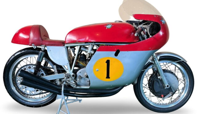 Vintage racing motorcycle with red top, blue side panel, and a yellow number 1 decal on the side panel, on a stand.