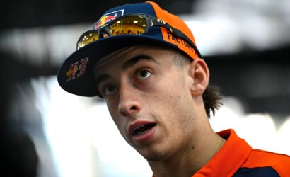 Young man wearing a blue and orange cap with sunglasses on the brim, looking upward in surprise or curiosity.