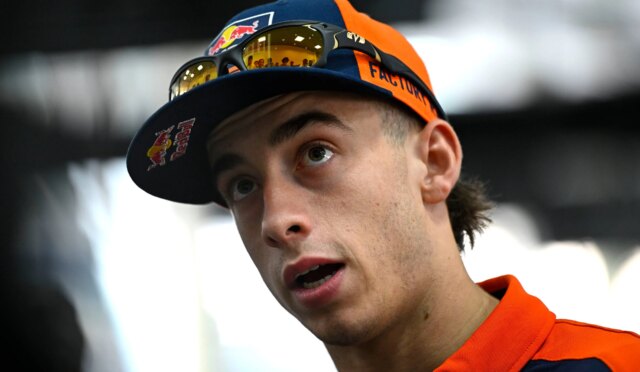 Young man wearing a blue and orange cap with sunglasses on the brim, looking upward in surprise or curiosity.