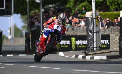 Racer on a red Honda motorcycle leaning into a turn, number 1, on a closed street with a crowd and Monster Energy banners in the background