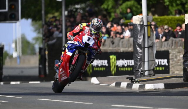 Racer on a red Honda motorcycle leaning into a turn, number 1, on a closed street with a crowd and Monster Energy banners in the background