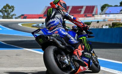 MotoGP rider in a red helmet on a blue Yamaha Monster Energy racing bike leaning into a corner on a race track.