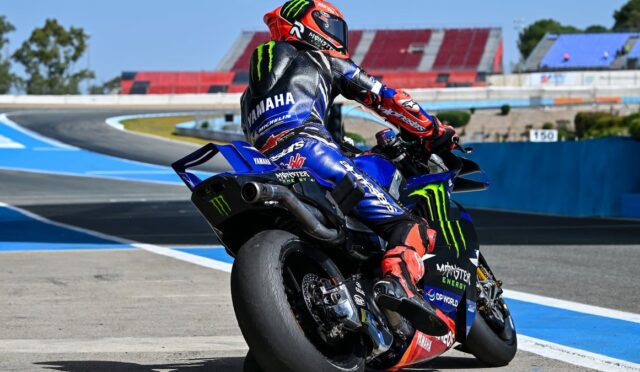 MotoGP rider in a red helmet on a blue Yamaha Monster Energy racing bike leaning into a corner on a race track.