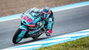Racing motorcycle #93 in turquoise-pink gear leaning into a corner on a race track.