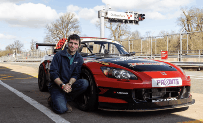 Man kneeling beside a red race car in the pit area at Oulton Park racetrack