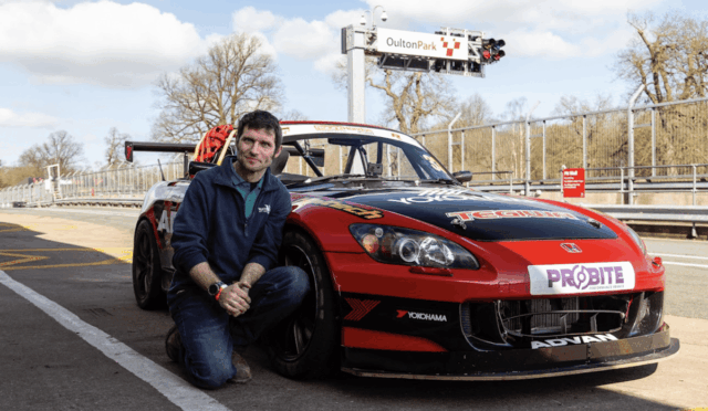 Man kneeling beside a red race car in the pit area at Oulton Park racetrack