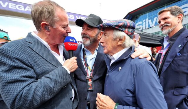 Reporter from Sky Sports interviewing an older man in a blue jacket at an outdoor event, with teammates nearby.