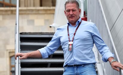 Man wearing a blue shirt and jeans stands on a metal outdoor staircase with a lanyard and ID badge around his neck.