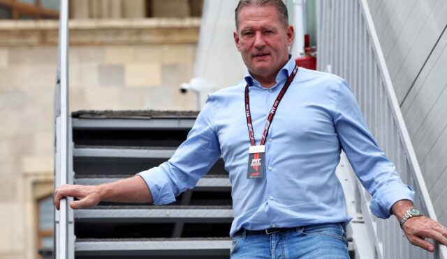 Man wearing a blue shirt and jeans stands on a metal outdoor staircase with a lanyard and ID badge around his neck.