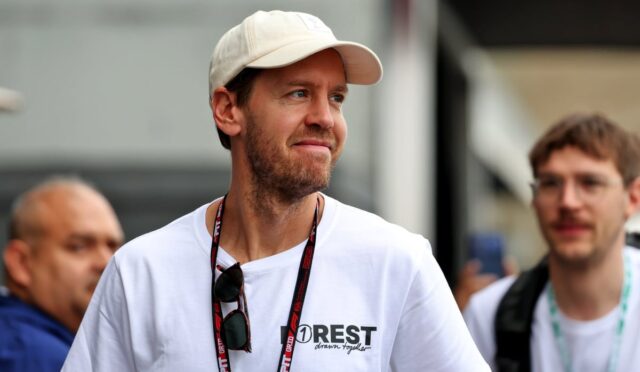 Man in a white cap and t-shirt with a lanyard, looking to the right at an outdoor event, sunglasses hanging from his shirt.