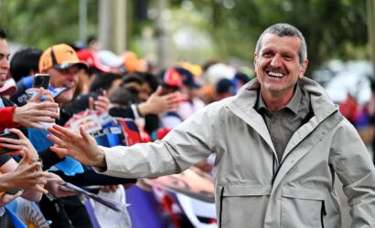 Smiling man in a light jacket extends his hand to high-five cheering fans at an outdoor event.