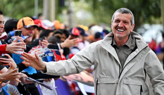 Smiling man in a light jacket extends his hand to high-five cheering fans at an outdoor event.