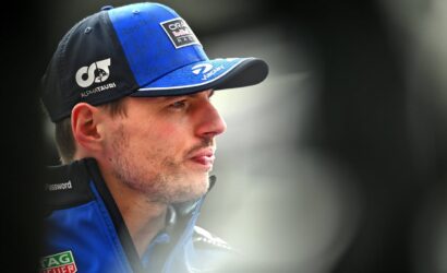 Close-up of a man in a blue racing cap and jacket, gazing to the right.