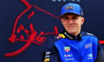 Portrait of a young race car driver in a blue Oracle Red Bull Racing jacket and cap, standing before a dark backdrop with a red Bull logo.