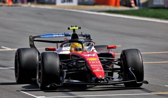 Red Ferrari Formula 1 car racing on a track, driver in a yellow helmet visible in the cockpit, large rear wing in view.