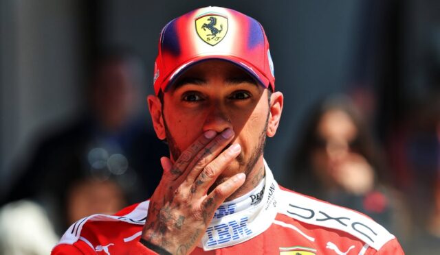 Portrait of a man in a red Ferrari cap, with his tattooed hand over his mouth during a moment at an event.