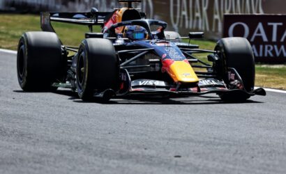 Red Bull Racing Formula 1 car speeding on a race track with large slick tires and a bright yellow nose cone, sponsor logos visible on the body.