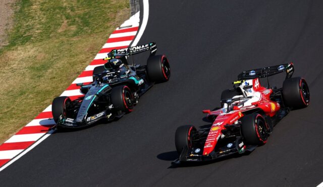 Two Formula 1 cars race side by side through a left-hand curve, a red Ferrari ahead of a dark Mercedes.