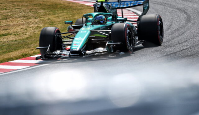 Teal Formula 1 race car cornering on a track, near red-and-white curbs with grass beside it.