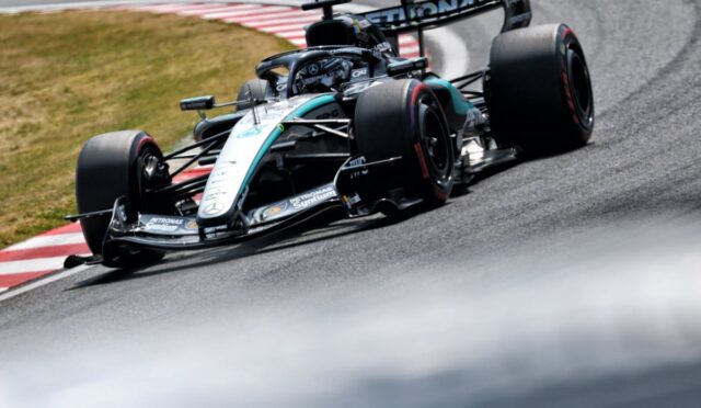 Mercedes Formula 1 car navigates a tight corner on a race track, tires gripping the red-and-white curbs.