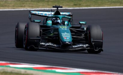 Green Formula 1 race car on a track, front view with sponsor logos visible and tires in motion on a curved section of the road course.