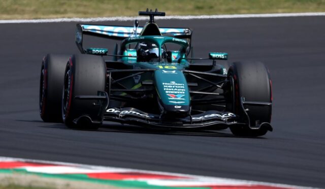 Green Formula 1 race car on a track, front view with sponsor logos visible and tires in motion on a curved section of the road course.