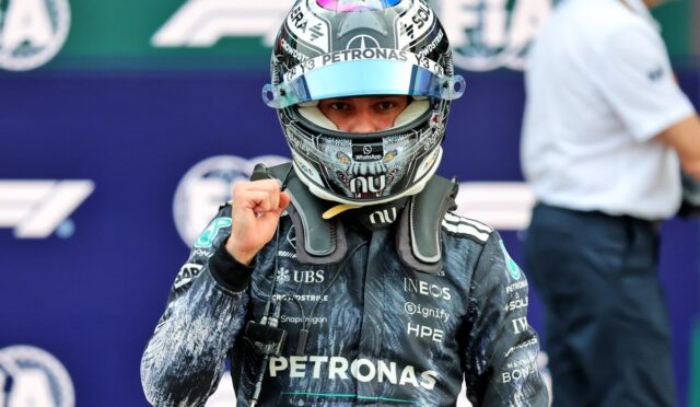 Formula 1 driver in a Petronas helmet and racing suit raises a clenched fist in celebration gesture on the grid.