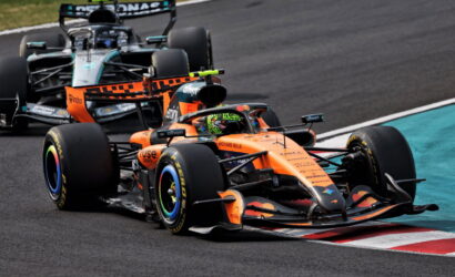 Orange McLaren Formula 1 car leading a tight corner, with a silver Mercedes close behind on the race track.