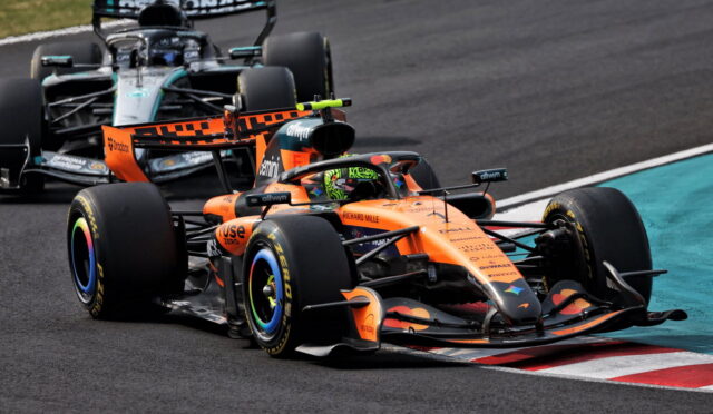 Orange McLaren Formula 1 car leading a tight corner, with a silver Mercedes close behind on the race track.