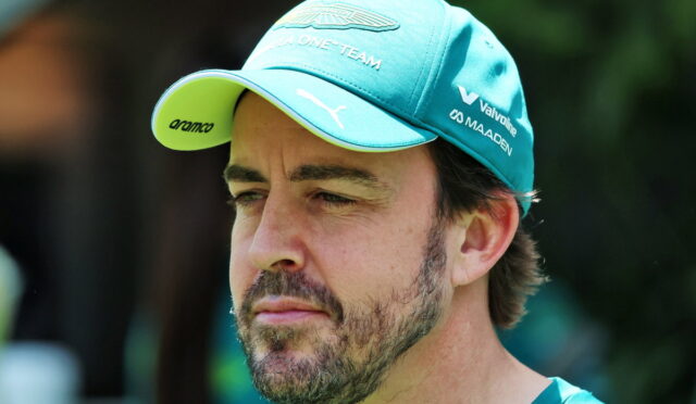 Close-up of a man with a teal cap and beard looking to the left, outdoors at a sunny event.