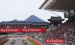 Race cars line up on a track as crowds watch from grandstands, with bold Fly Emirates banners overhead.