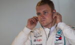 Formula One driver in a white racing suit adjusting earphones, focused on the headset.