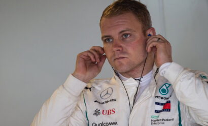 Formula One driver in a white racing suit adjusting earphones, focused on the headset.
