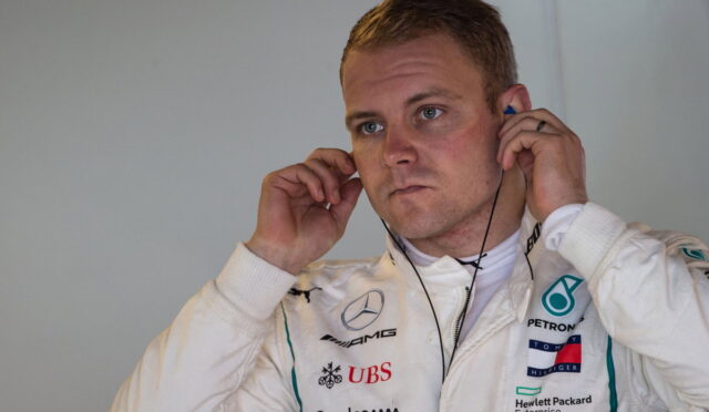 Formula One driver in a white racing suit adjusting earphones, focused on the headset.